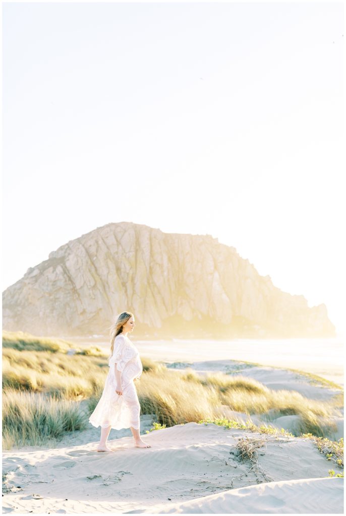 Pregnant woman walking in the sand with Morro Bay rock behind her