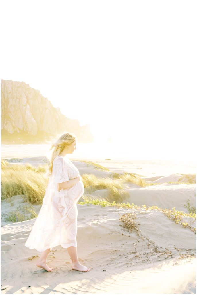Woman walking in the wind at the beach in maternity dress.