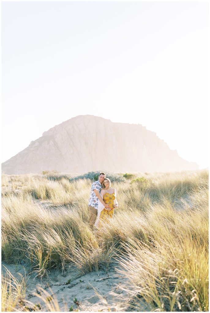 Couple hugging in the tall grass and sand during beach maternity photos