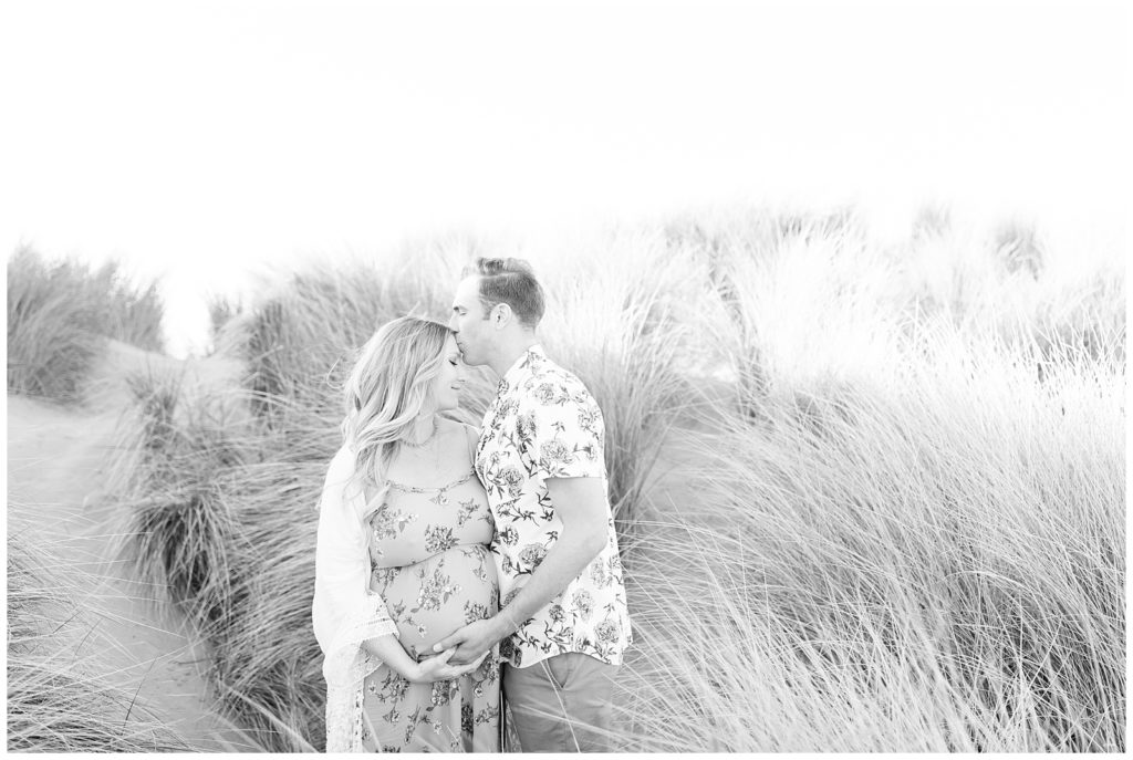 Couple standing in tall grass while husband kisses wife's forehead