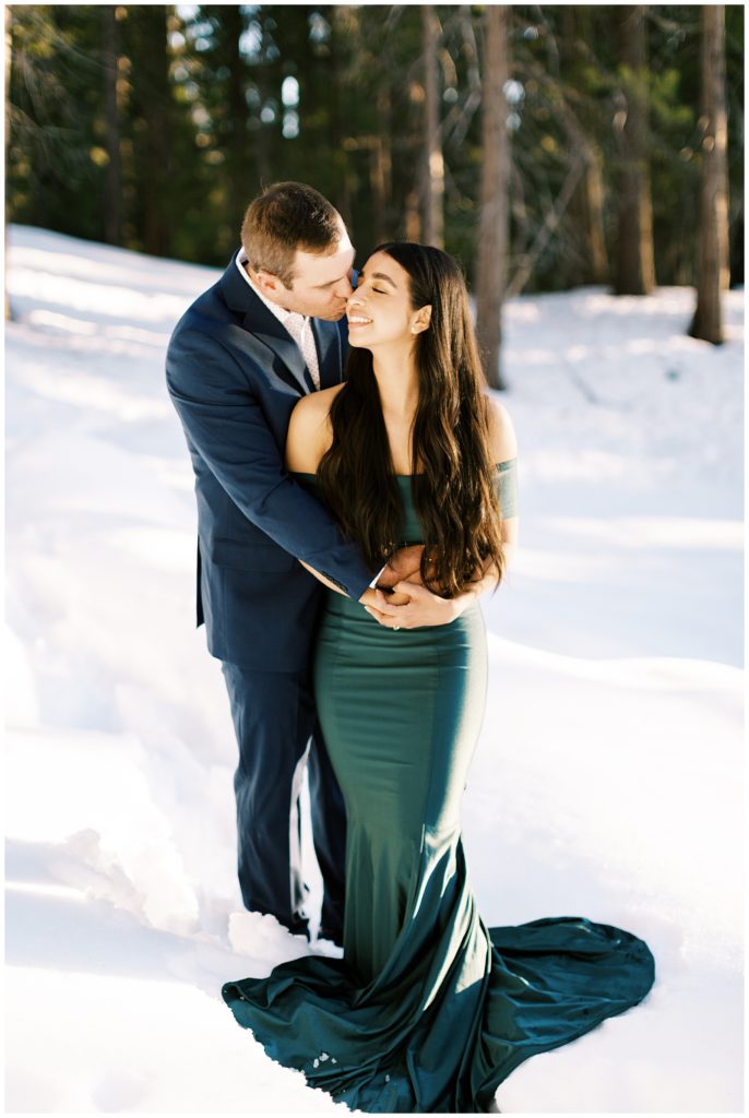 Man hugging woman in green dress while standing in snow