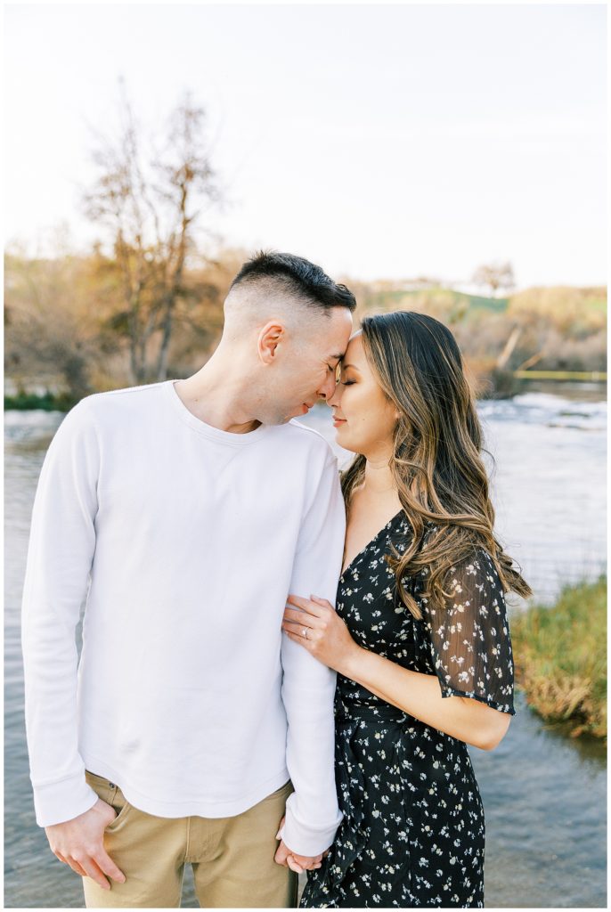 Engaged couple in front of Lost Lake forehead to forehead. 