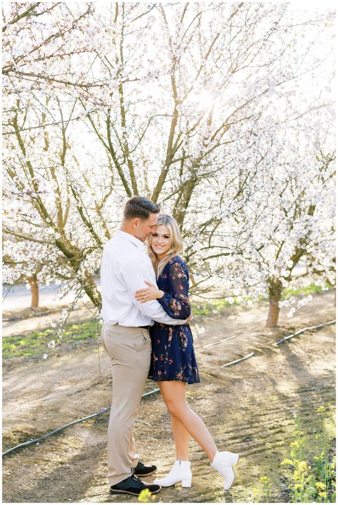 Engaged couple standing in front of white blossom tree for spring engagement photos by fresno wedding photographer megan helm photography