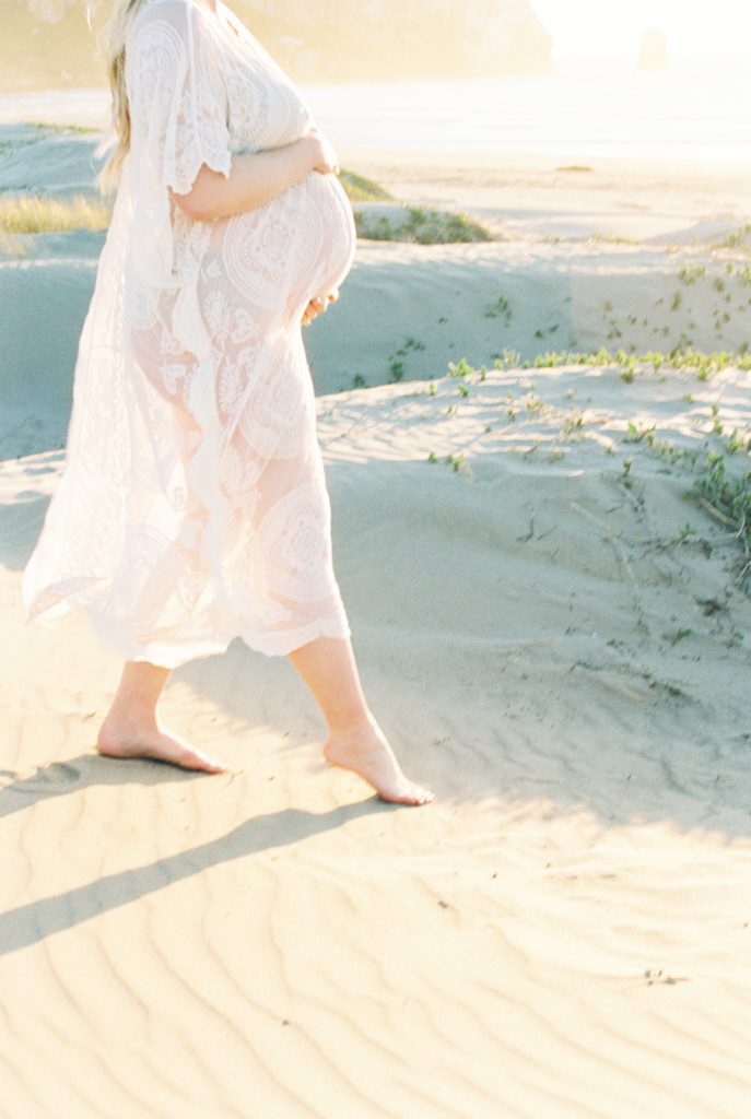 Film photo of pregnant woman walking in sand holding her belly