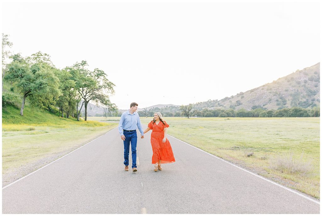 Couple walking down the street among wildflowers holding hands at sunset during engagement photos