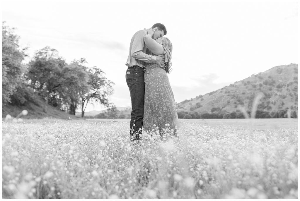 Engaged couple kissing while standing in a field of wildflowers during engagement photos