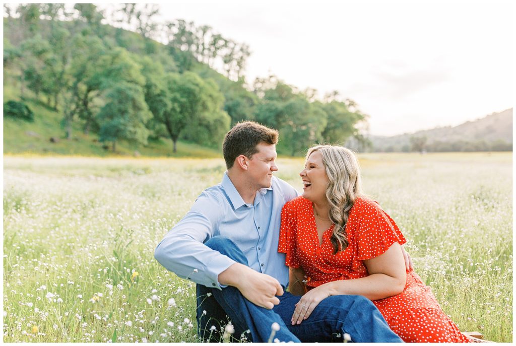 Couple sitting in wildflowers laughing for engagement photos