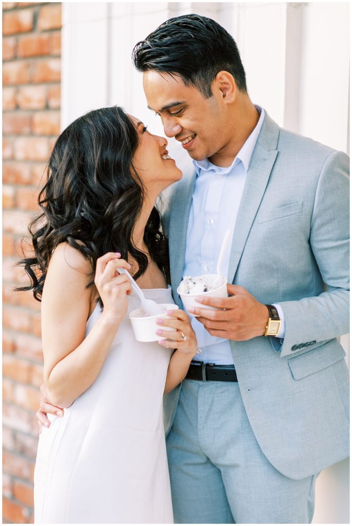 Engaged woman leaning up to kiss fiance in blue linen suit. 