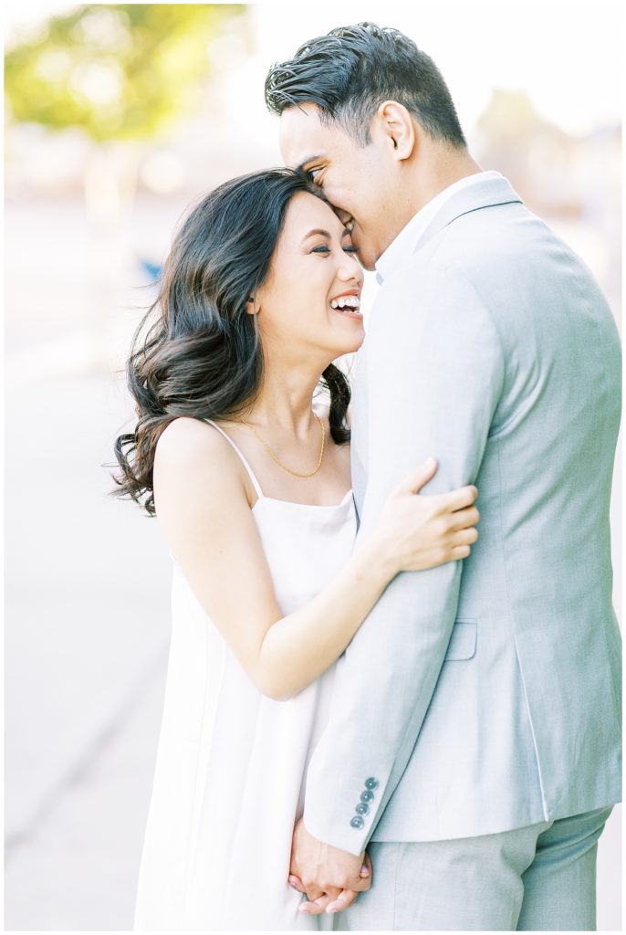 Woman laughing while fiance in linen suit jacket whispers to her
