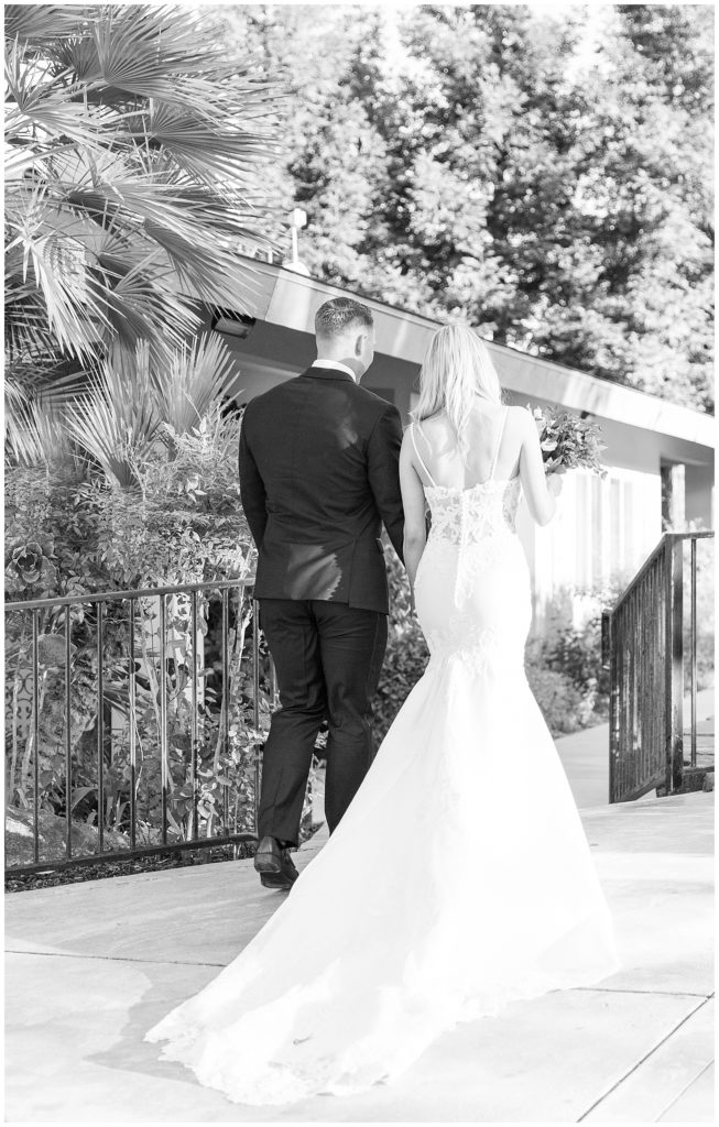 black and white photo bride and groom walking away holding hands