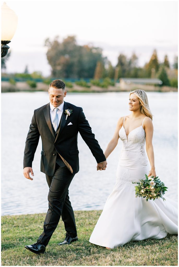 groom leading bride holding her hand walking by lake