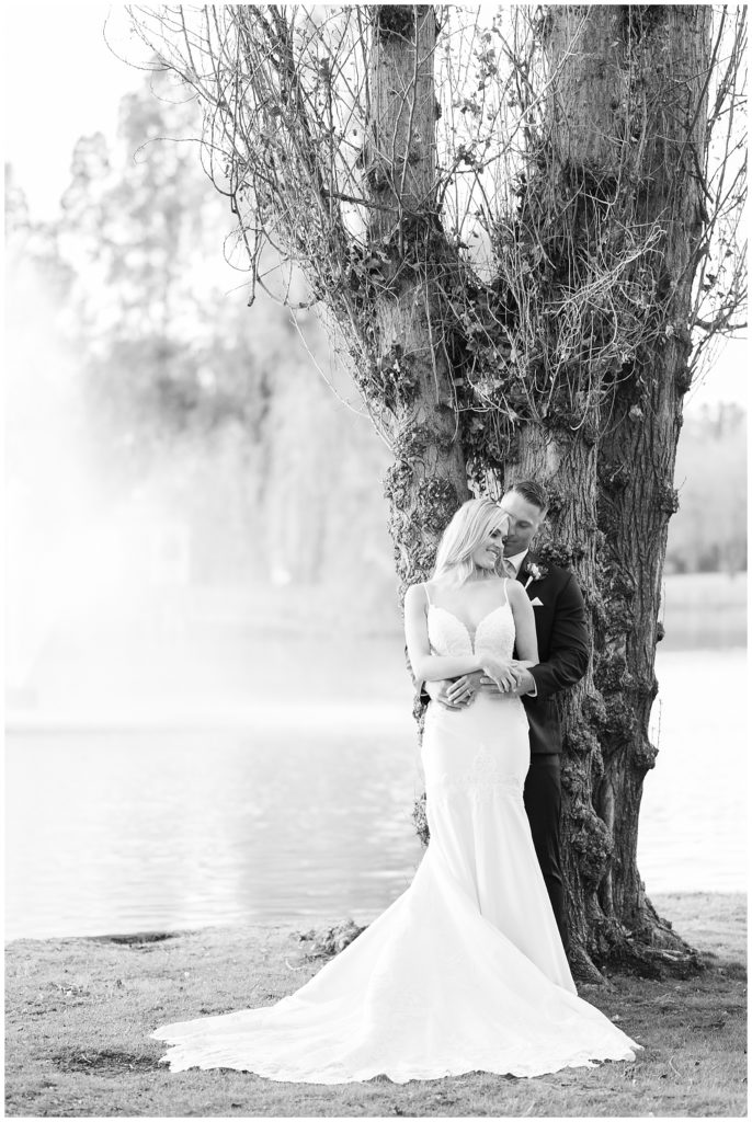 black and white photo of a bride and groom embracing by a tree