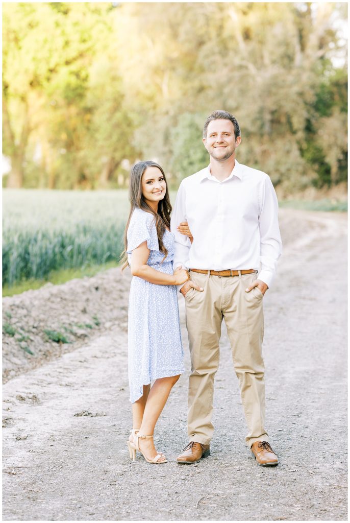 Engagement photo in dirt road with woman in blue spring dress and man in beige slacks. 