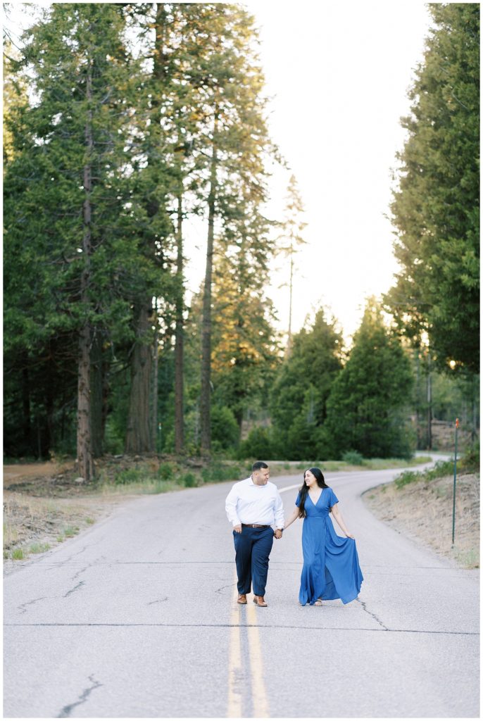 engaged couple wearing dress clothes holding hands and walking along an empty mountain road