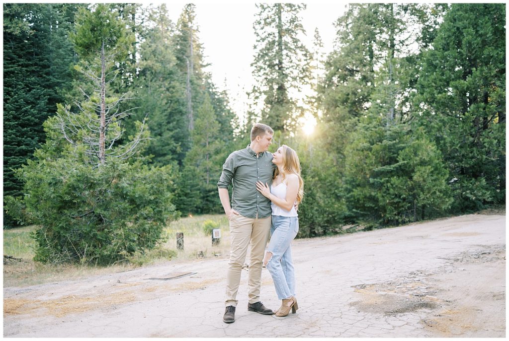engaged couple standing along a dirt trail in the mountains of shaver lake with golden sunlight shining behind them