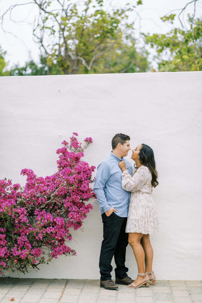 engaged couple embracing in front of a white stone wall with a pink bougainvillea in Monterey California