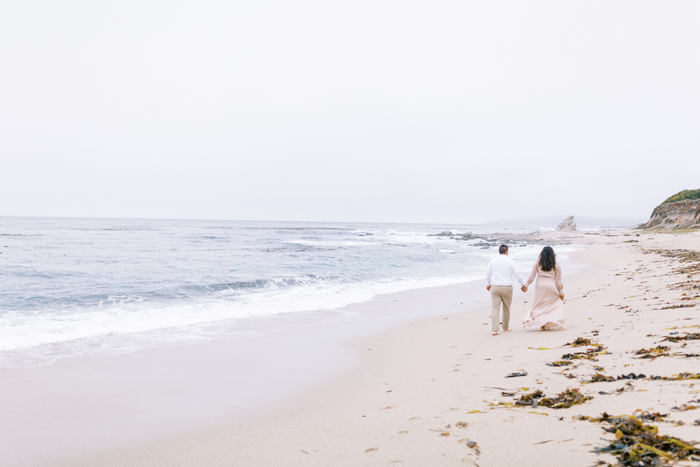 couple holding hands and walking along the beach on a foggy coastal day in California