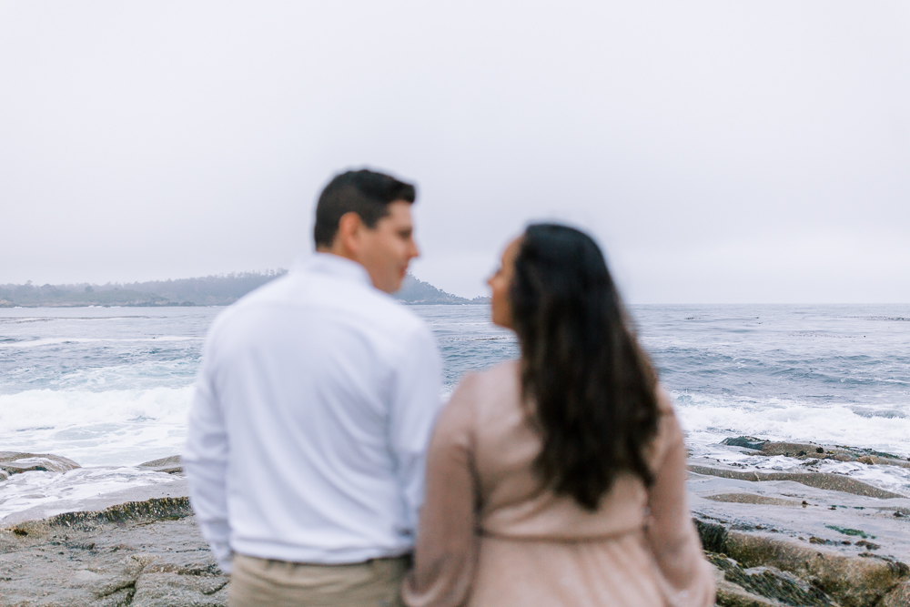 blurry photo of a couple standing on a rocky beach looking at eachother with the horizon in focus
