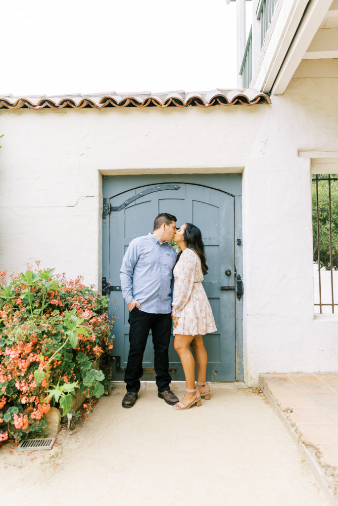 engaged couple kissing in front of a blue door