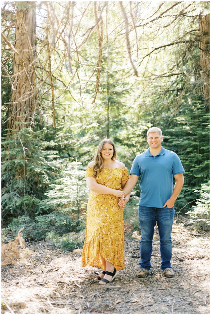 man and woman holding hands and smiling in yellow dress and blue shirt fresno engagement photographer shaver lake