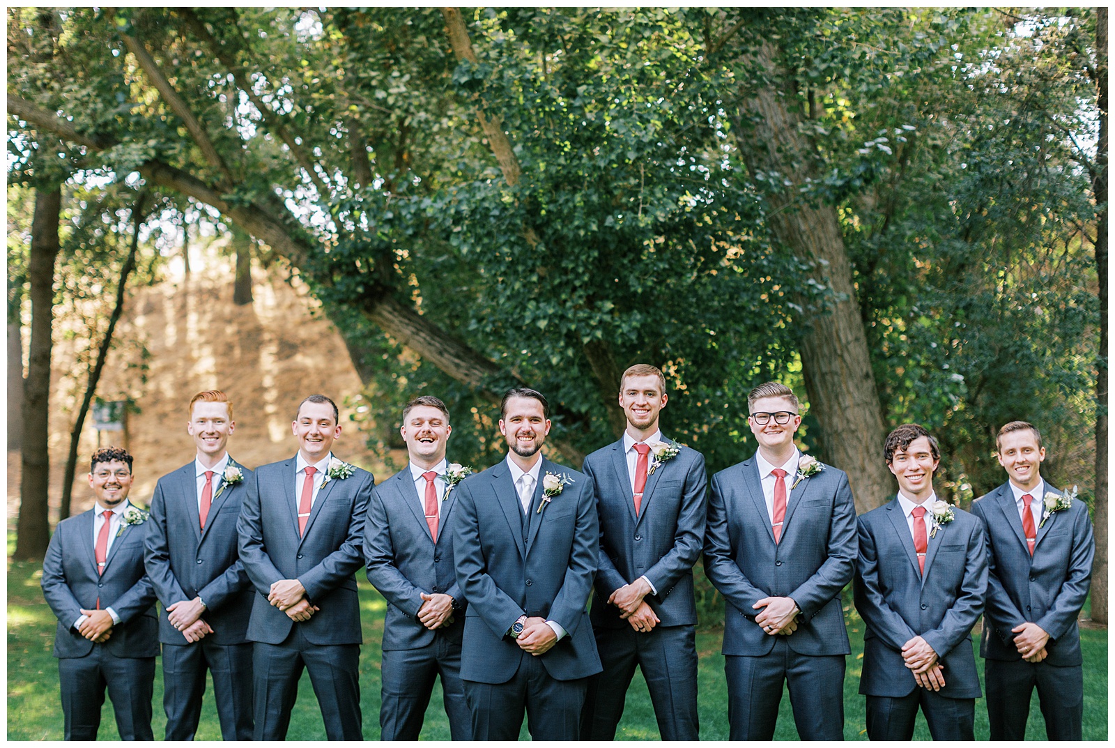 groom and groomsmen flying v pose smiling grey suits with rust colored ties