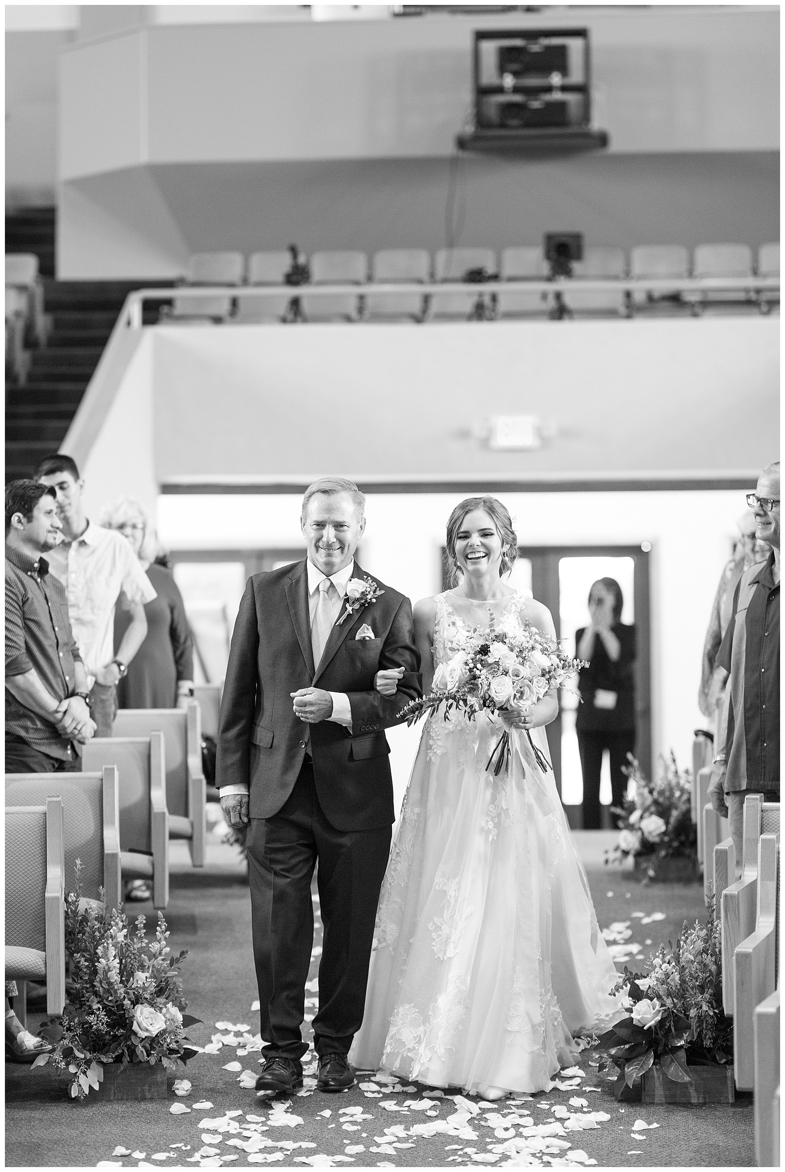 bride smiling walking with dad down church aisle black and white