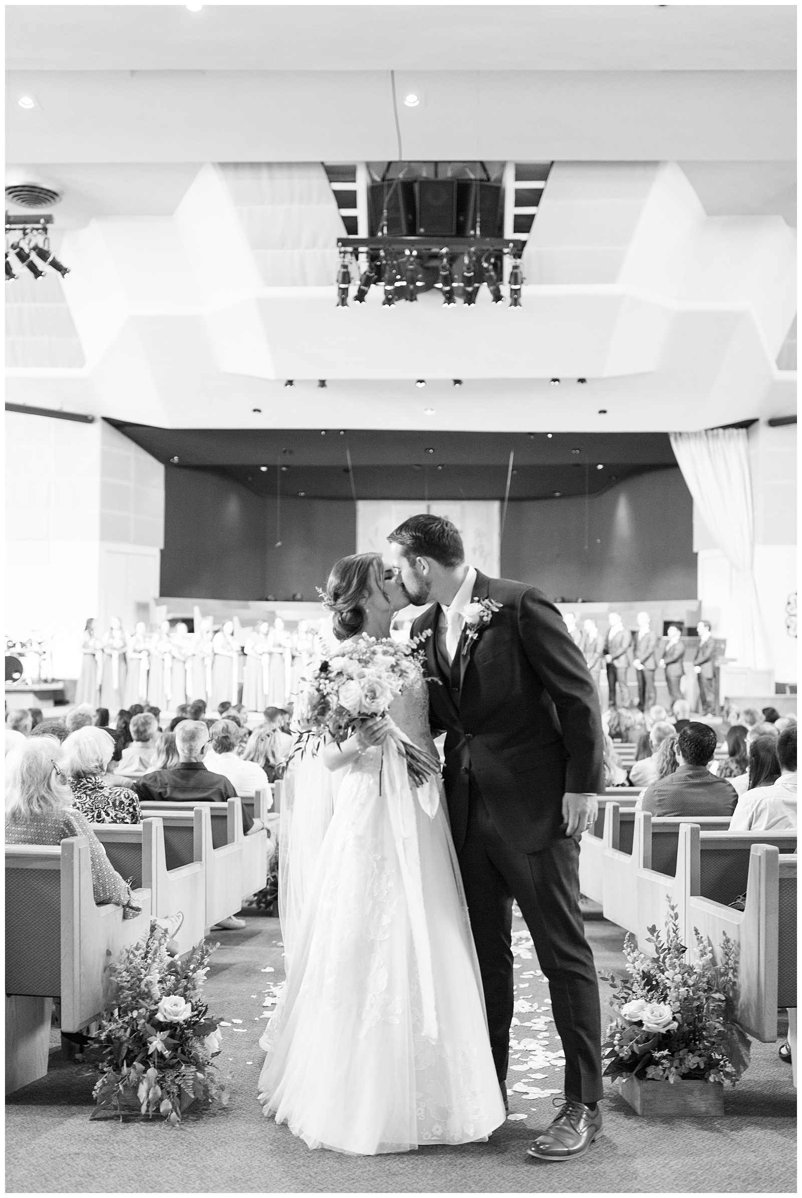 black and white image bride and groom kissing at end of aisle church wedding ceremony