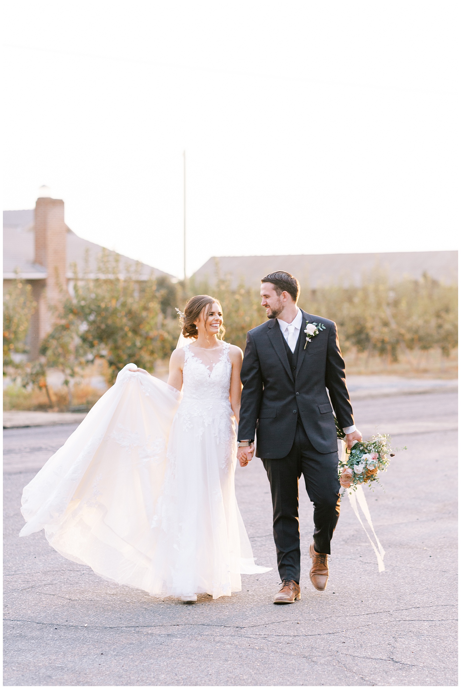 bride and groom walking and holding hands bride holds wedding dress groom holds bouquet