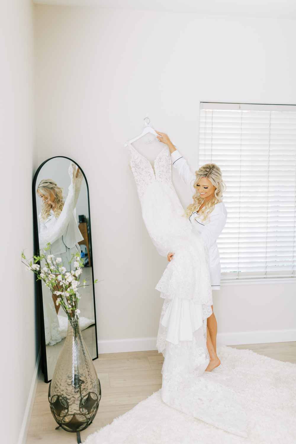 bride in white pajamas hanging up wedding dress smiling