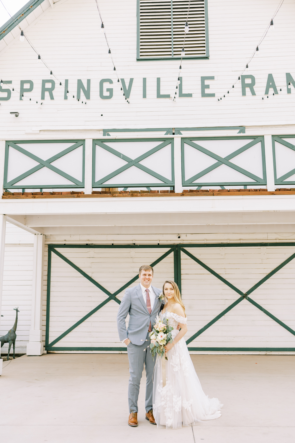 bride and groom in front of white barn at springville ranch