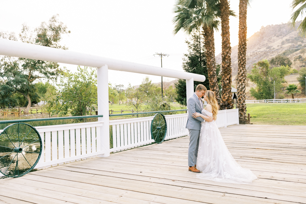 bride and groom embracing on bridge palm trees and golden sunset glowing behind them at springville ranch wedding
