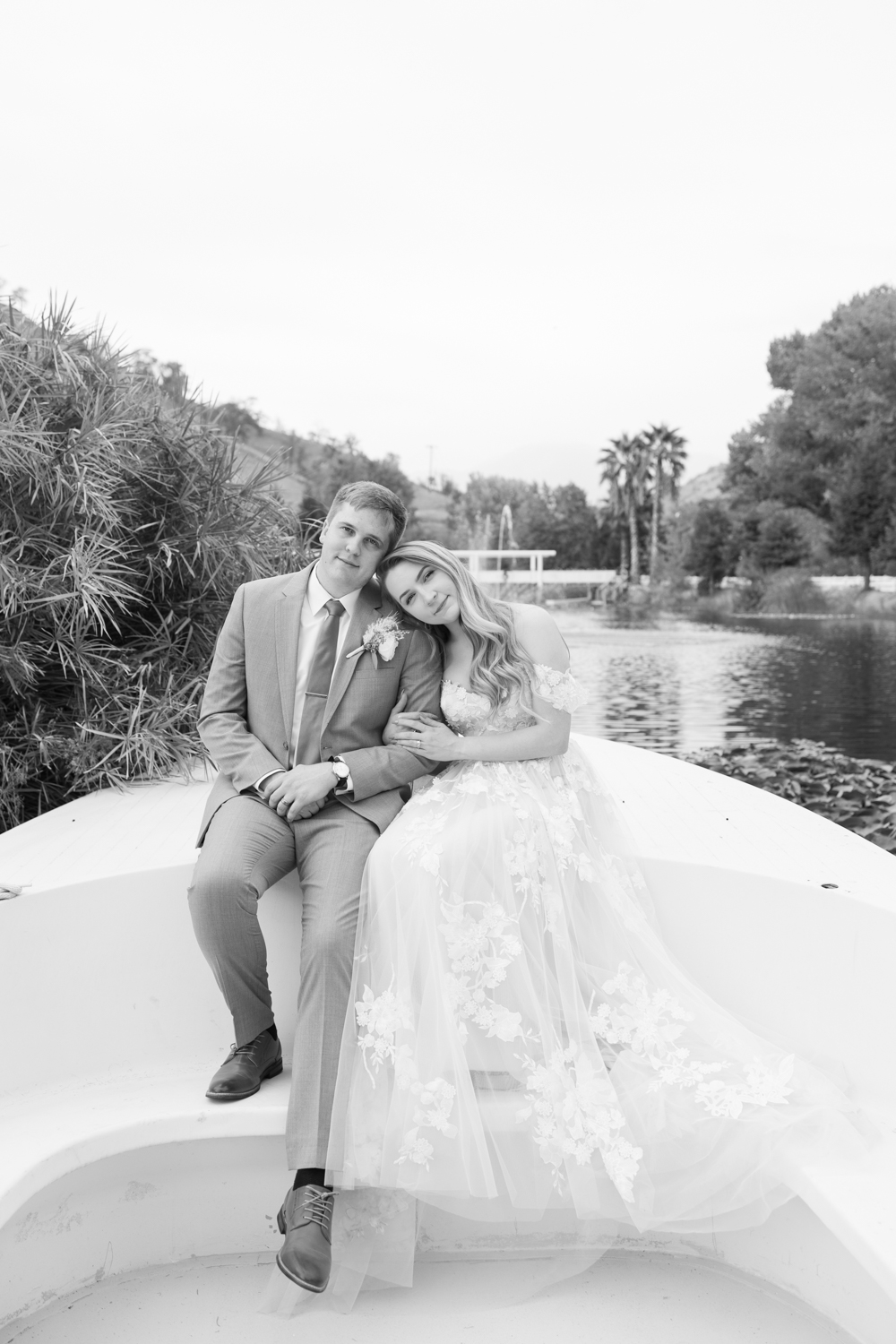 black and white photo bride and groom sitting on boat bride resting head on grooms shoulder lake in background at springville ranch