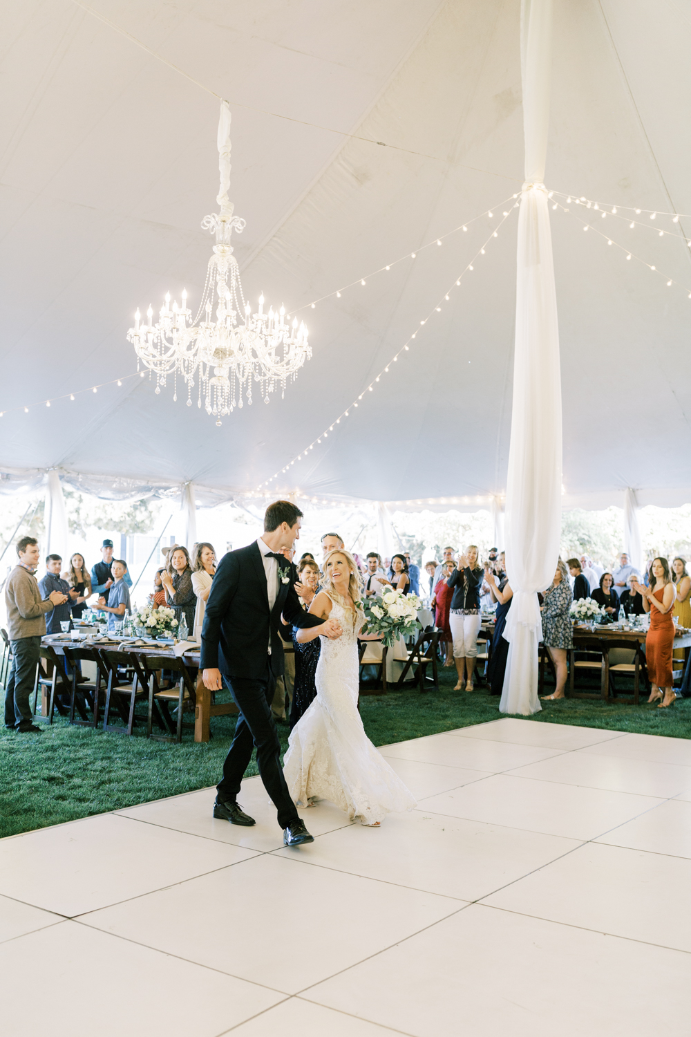 bride and groom holding hands walking onto dance floor in white tent