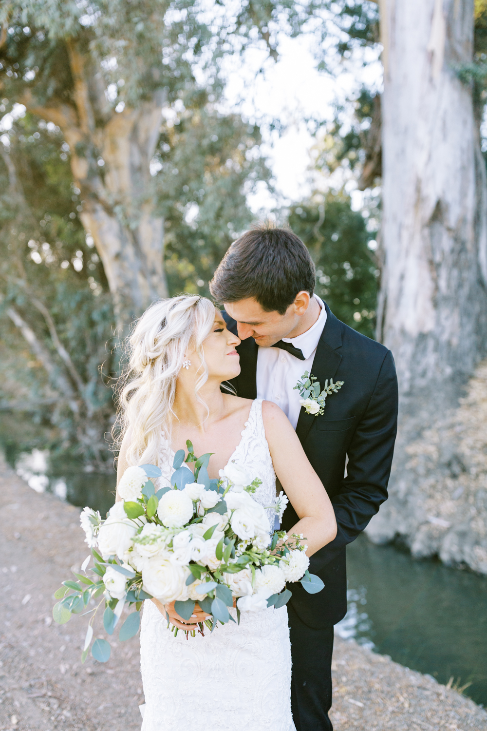bride and groom nuzzling noses and smiling bride holding white and green wedding bouquet