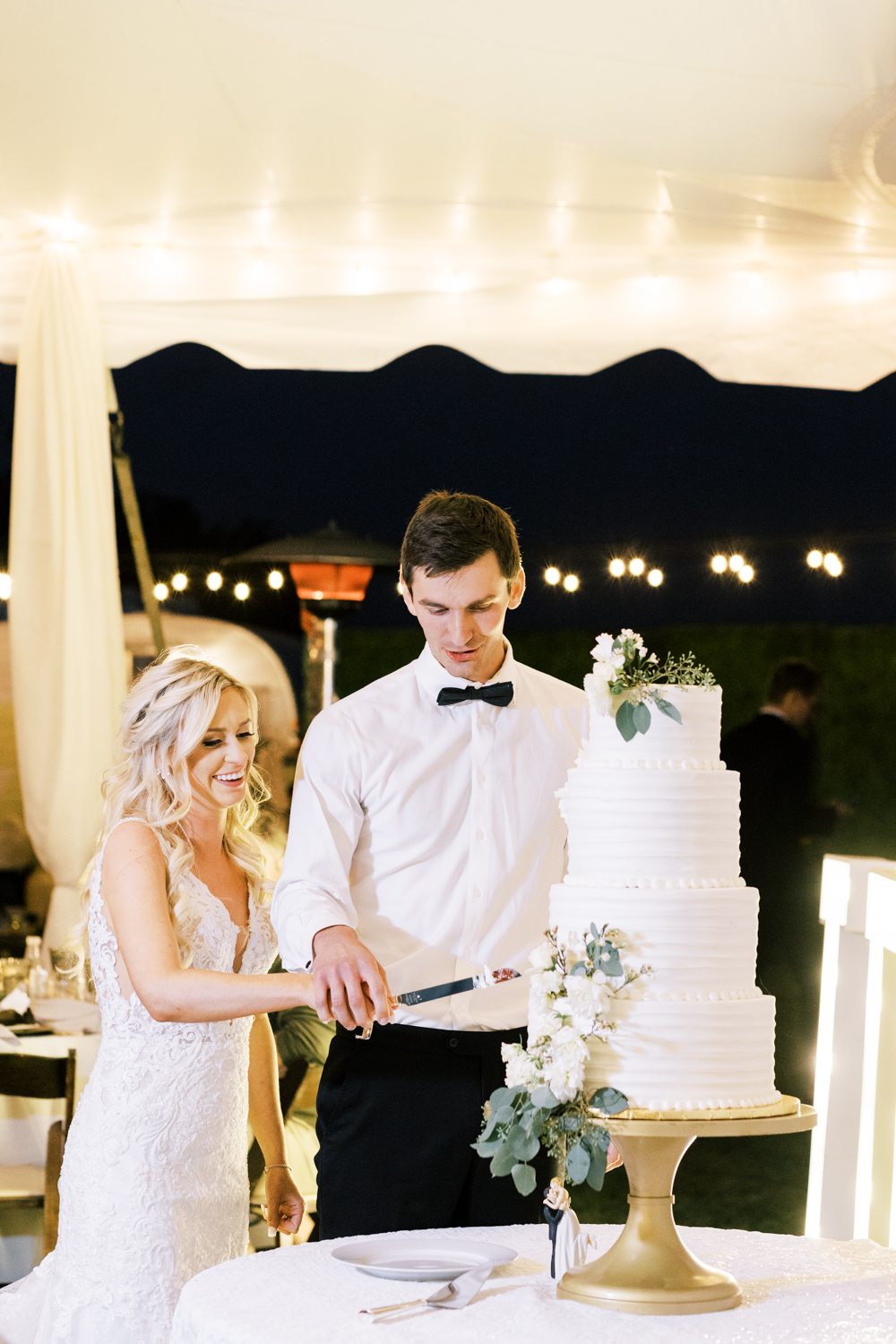 bride and groom cutting four tier white wedding cake elegant backyard wedding under white tent