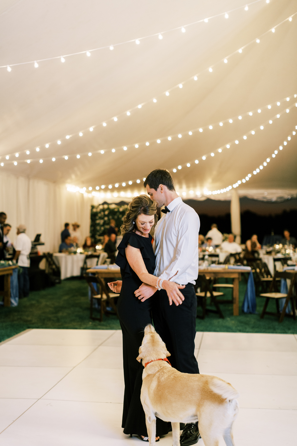 groom dancing with his mother and dog under tent at wedding reception