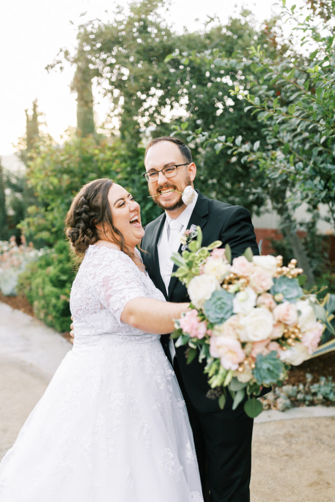groom with flower in mouth laughing and bride smiling at the gardens venue in tulare