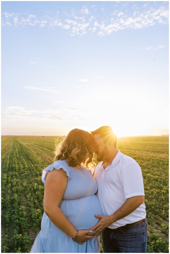 man and woman embracing in alfalfa field with sunlight shining