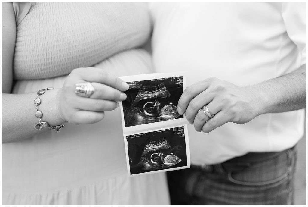 close up black and white photo of man and woman holding sonogram photos of baby