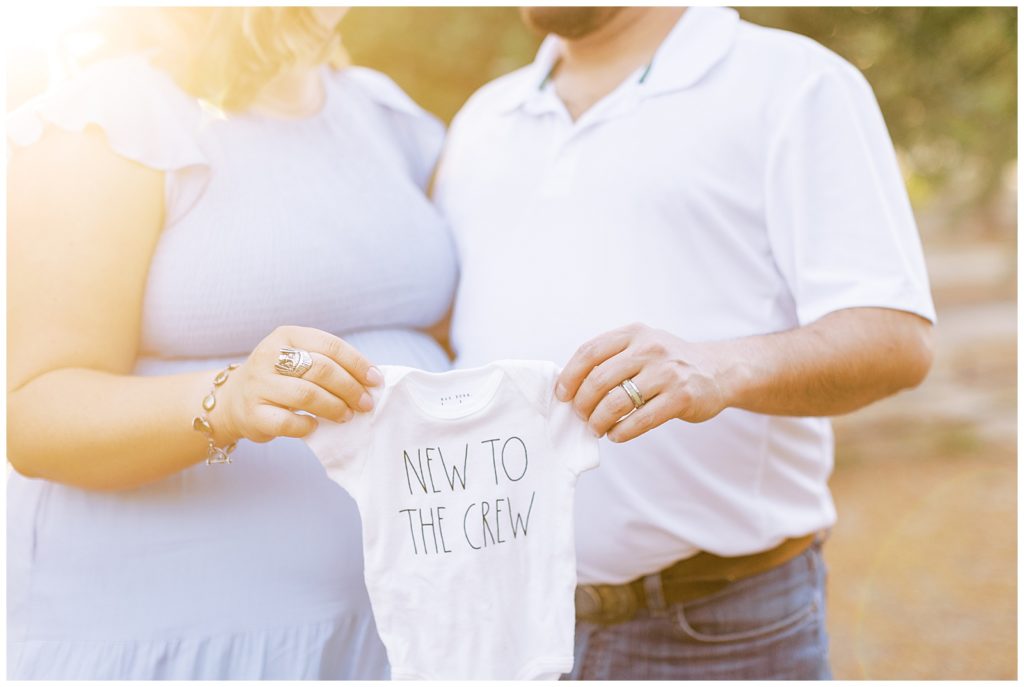 close up of dad and pregnant wife holding baby onesie for maternity photos