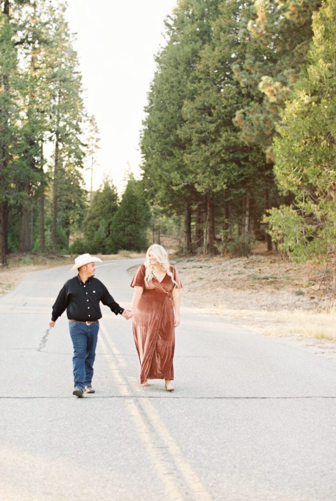 man and woman holding hands walking along road in shaver lake