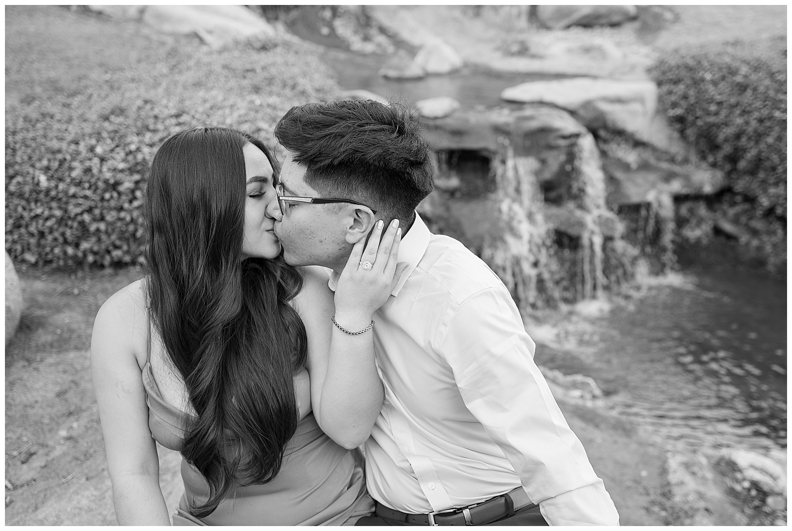black and white photo engaged couple kissing waterfall in background