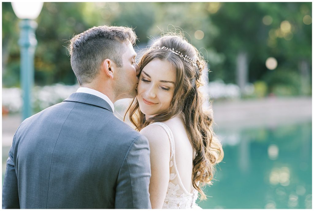 groom kissing bride on the cheek by a lake wonder valley wedding