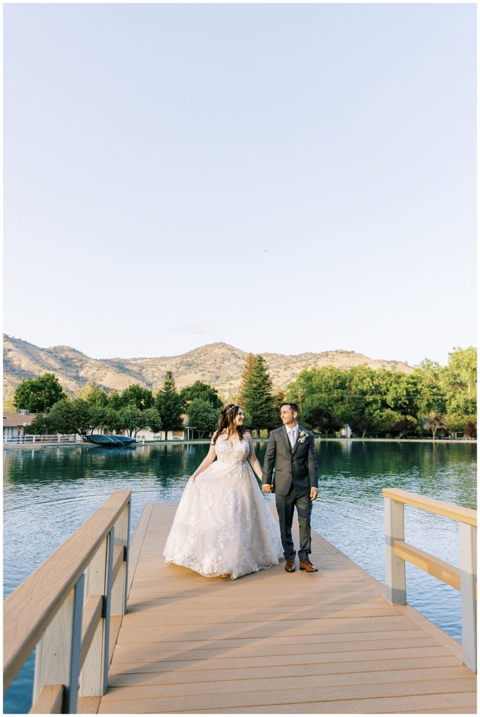 bride and groom walking on dock on a lake sunset