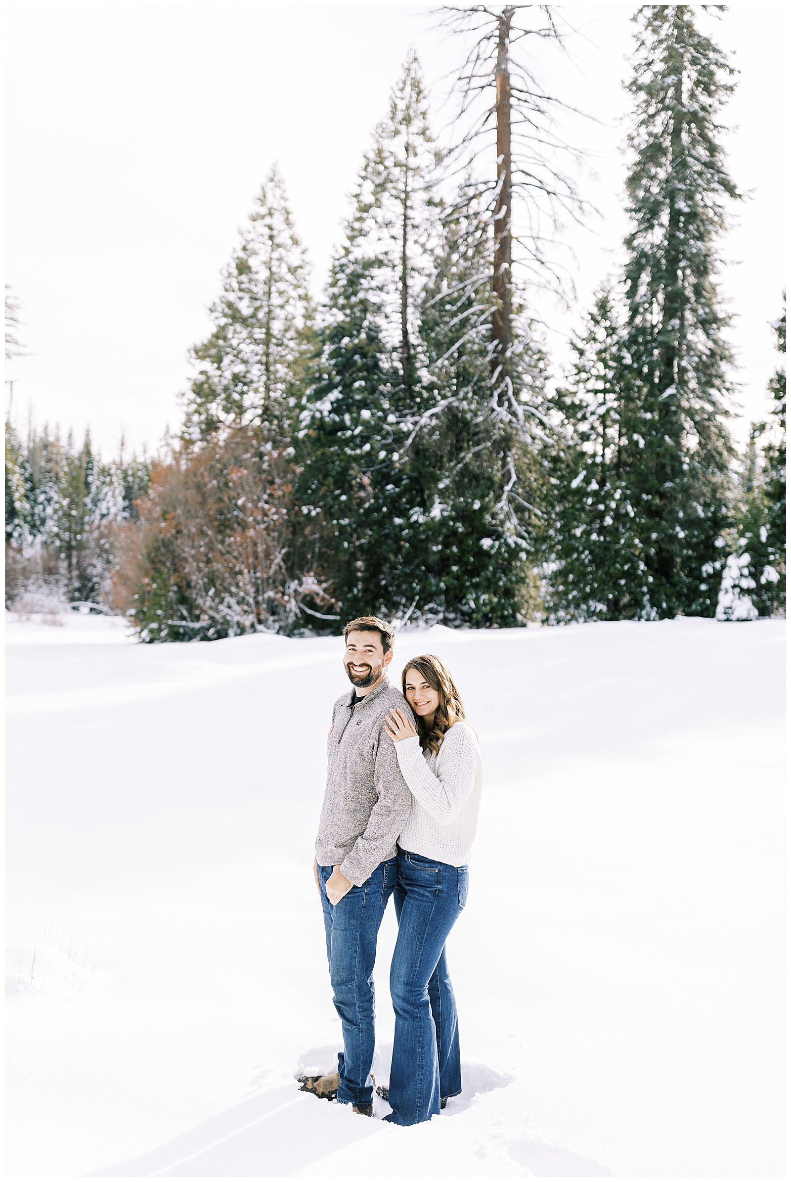 engaged couple embracing in snowy mountain meadow