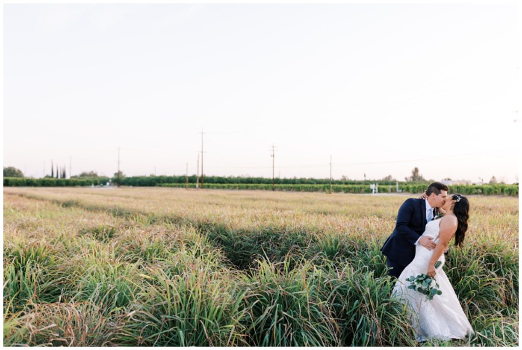 groom dipping bride for kiss in field at sunset