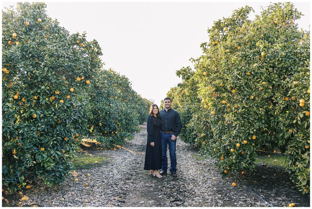 man and woman hugging and smiling in orange grove wearing black engagement photos