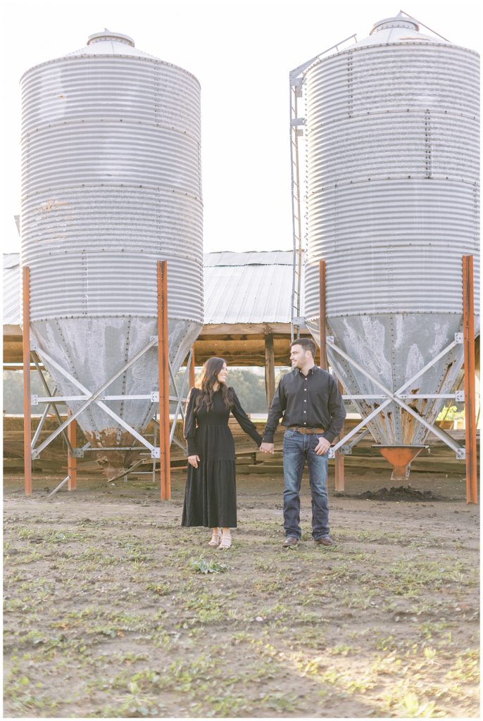 engaged couple holding hands in front of metal silos