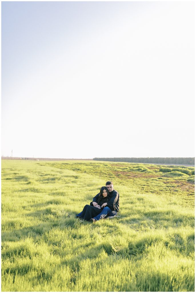 man and woman sitting and embracing in green grass field at sunset