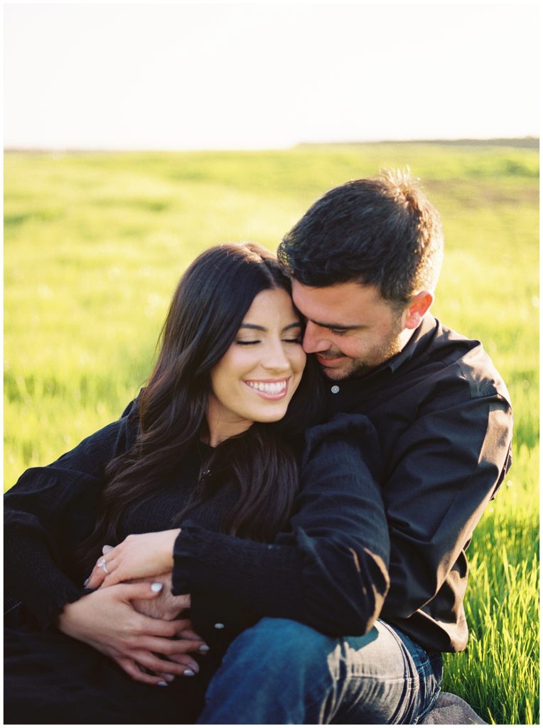 man and woman sitting in green grass field dutton ranch inspired engagement photos sunset